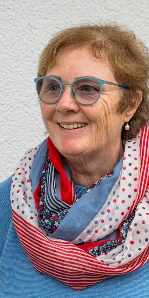 Gisela Maria Schmid lächelt mit rotem Schal und blauer Brille